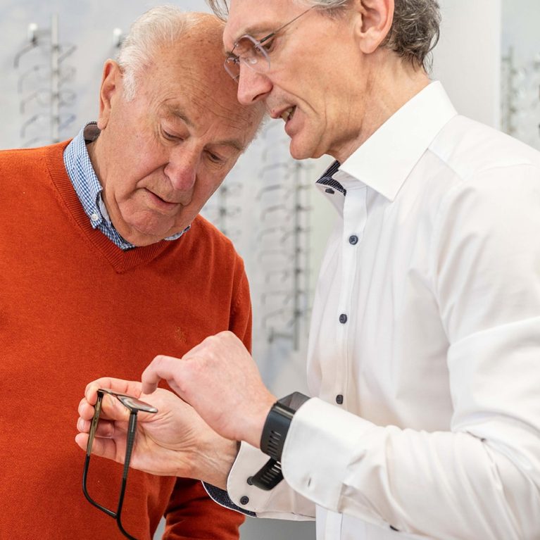 Optiker zeigt Kunden eine Brille und erklärt etwas